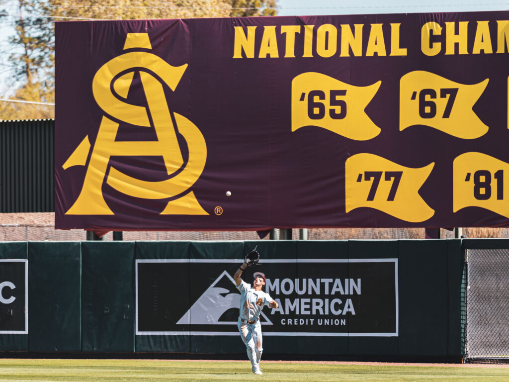 Kien Vu fields a ball in the outfield in front of ASU's towering National Champions signage. (Photo by Joshua Eaton/Sun Devil Daily)